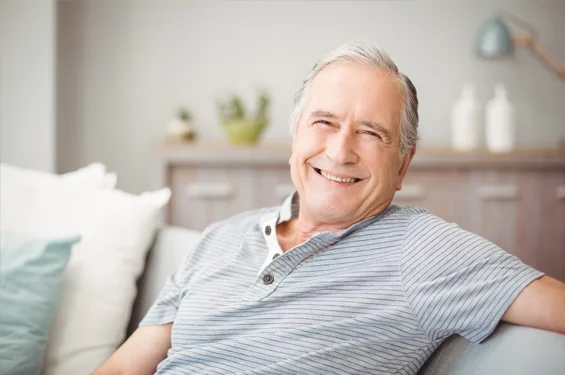 Smiling older man relaxing on couch in comfortable home setting, wearing striped shirt.