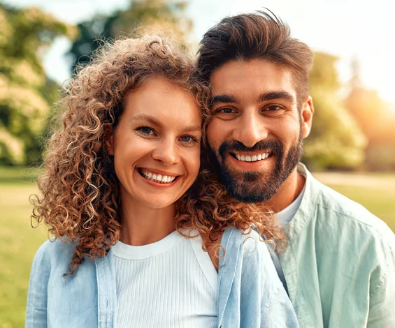 Happy couple smiling outdoors in park setting, showcasing healthy teeth and bright smiles.
