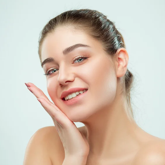 Young woman touching her face, smiling, demonstrating healthy skin and dental care wellness against white background.