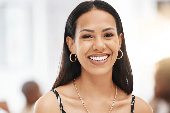 Smiling woman wearing hoop earrings in bright dental office setting with blurred background
