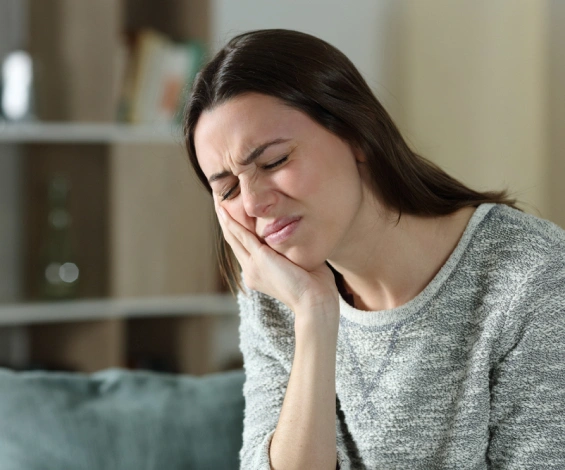 Woman with hand to face experiencing tooth pain in home setting