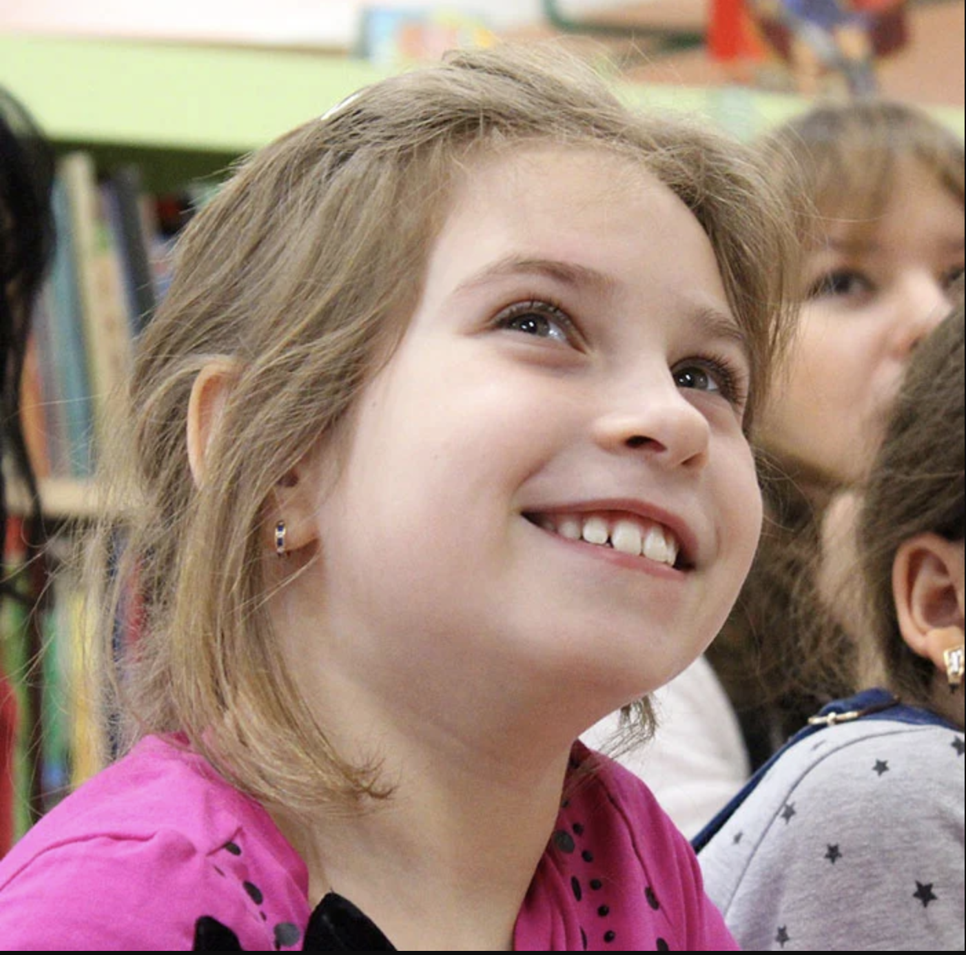 Young girl smiling brightly in classroom setting, displaying healthy teeth and happy expression.