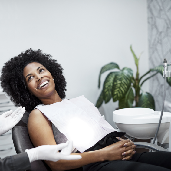Woman smiling while holding dental documents in bright office with plant.