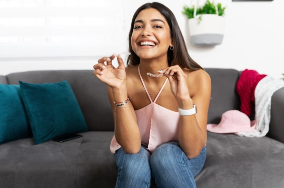 Smiling woman holding dental floss on couch in modern living room setting.