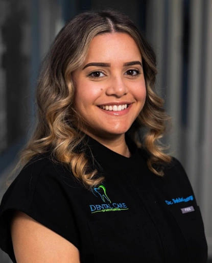 Young woman in black dental scrubs smiling at camera in professional dental office setting.