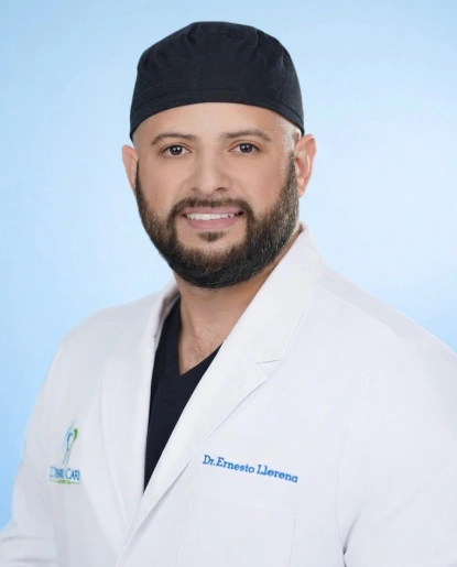 Male dentist in white coat and black headband smiling at camera against blue background.
